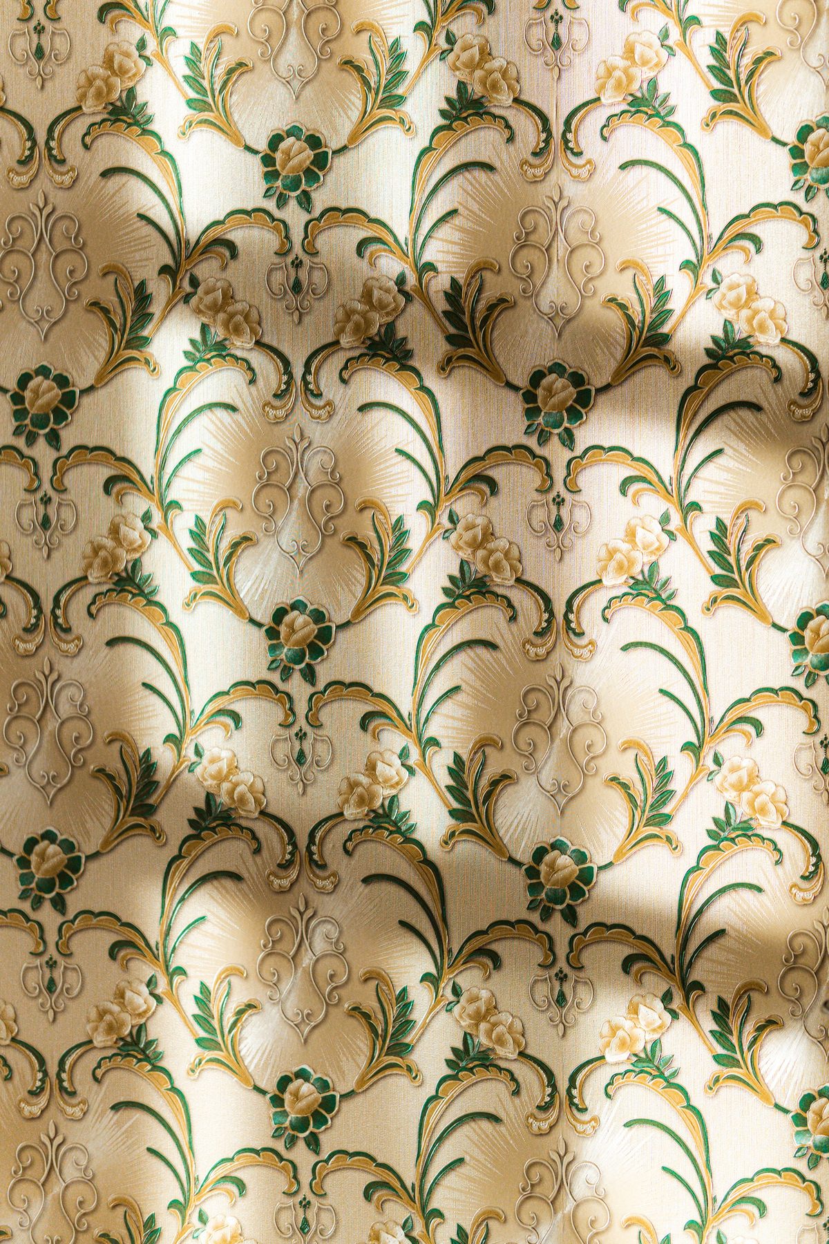 Close-up of cream wallpaper with green and gold floral scrollwork catching raking sunlight