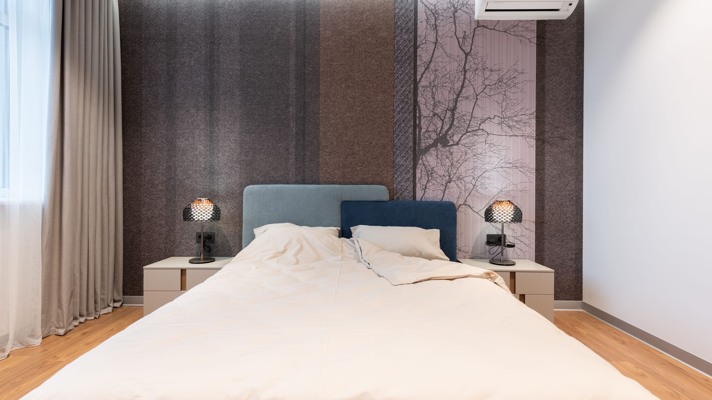 Modern bedroom with a full-height wall of textured panels and a soft tree-silhouette mural behind blue upholstered headboards